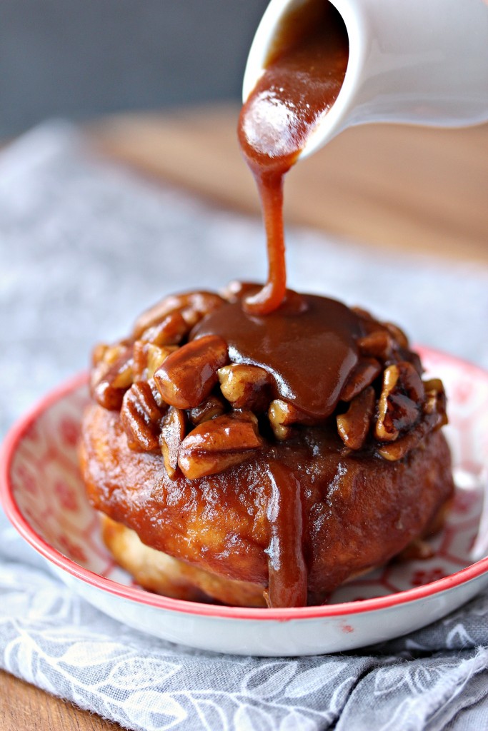 Overnight Apple Pecan Caramel Sticky Bun on a small plate with caramel being poured over top of it. 