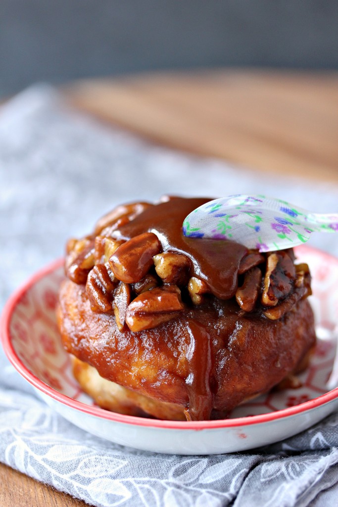 Overnight Apple Pecan Caramel Sticky Buns served in a small plate, a small colourful spoon is taking a scoop out of the bun