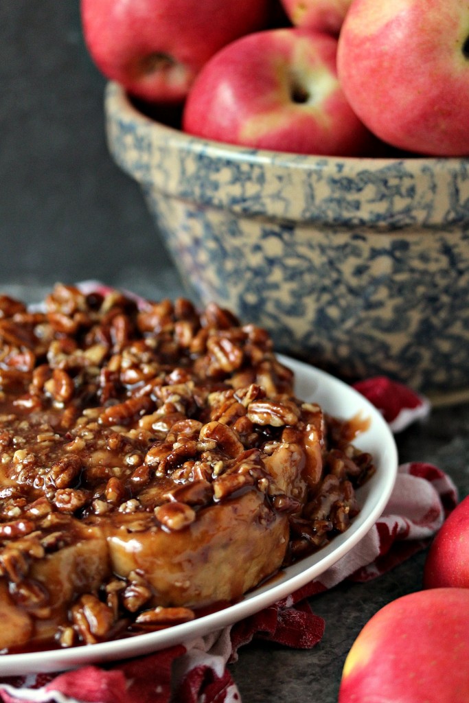 Overnight Apple Pecan Caramel Sticky Buns served on a white plate with a bowl of apples in a blue bowl behind it