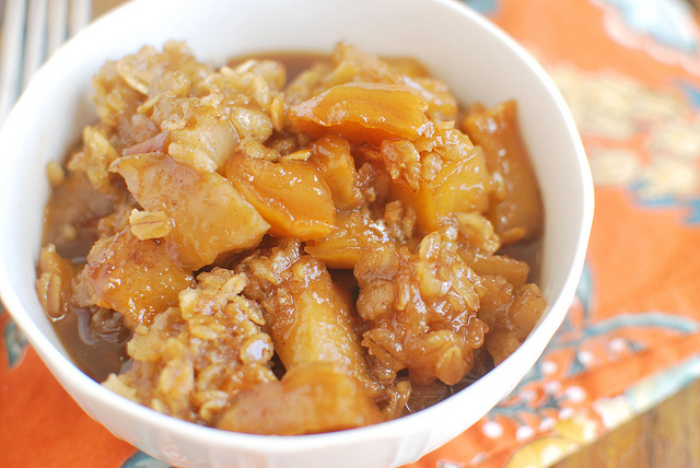 Slow Cooker Caramel Apple Crumble – Fake Ginger recipe image of finished crumble in a white bowl on an orange printed napkin.