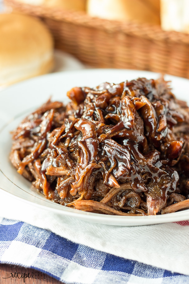 Slow Cooker Honey Balsamic Pulled Pork – The Recipe Rebel image of finished recipe in a white serving dish on a blue and white checkered napkin,
