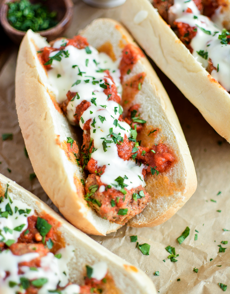 Slow Cooker Meatball Subs with Parmesan, White Cheddar Queso – Cooking and Beer image of finished recipe on parchment paper with fresh herbs scattered around