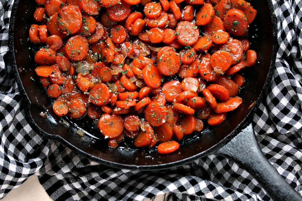 Honey Glazed Carrots in a cast iron pan resting on a black and white checkered napkin.