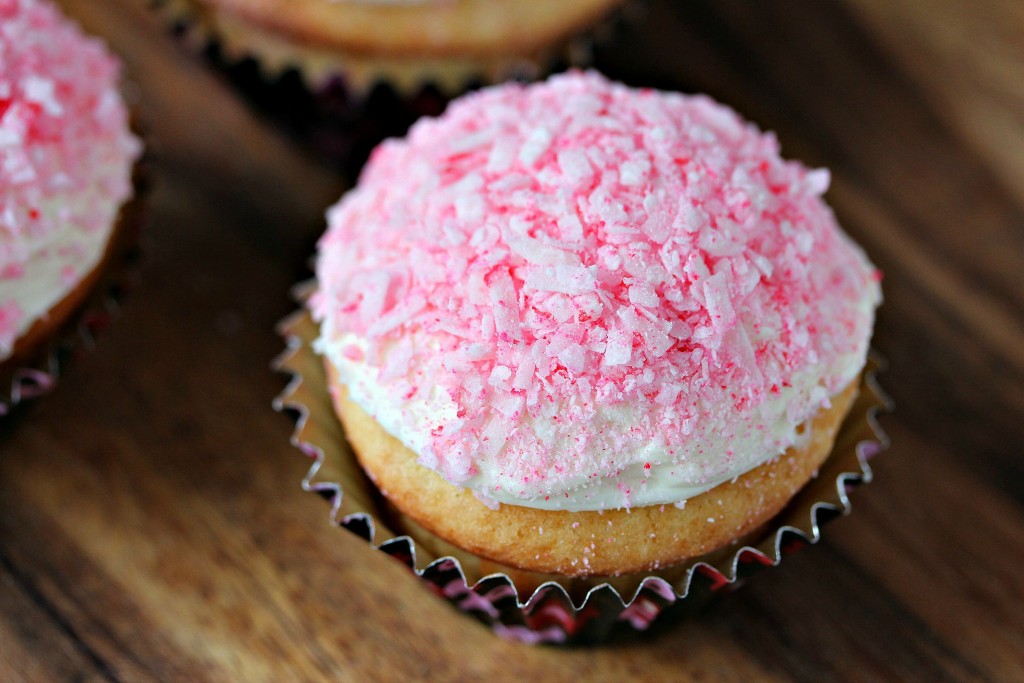 cupcakes on a counter with pink coconut on top of the frosting