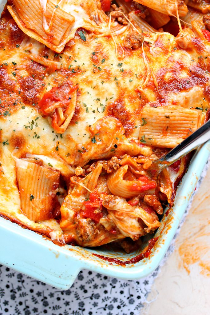 Easy Cheesy Pasta Bake with Sausage and Peppers in a blue casserole dish with a spoonful being taken out.