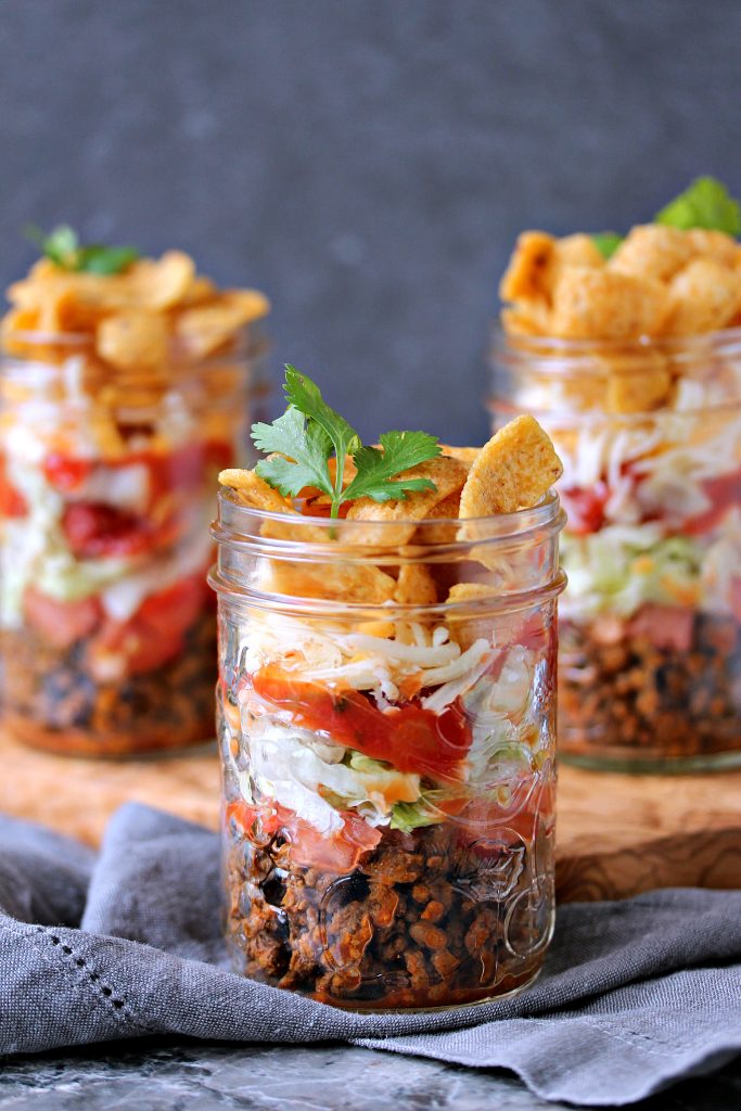 Mini Fritos Taco Salads layered in mason jars sitting on a wood platter on a tabletop
