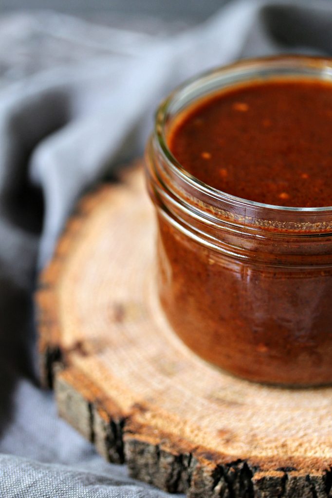 close up image of easy homemade enchilada sauce in a mason jar sitting on a wood trivet on a grey napkin 