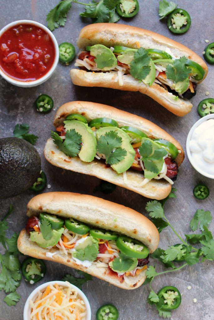 Mexican Hot Dogs are grilled to perfection, then topped with jalapeno peppers, salsa, cheese, sour cream and avocados. This recipe is a real crowd pleaser. (@CravingsLunatic)