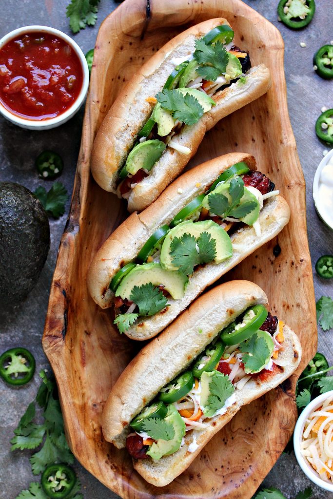 Mexican Hot Dogs are grilled to perfection, then topped with jalapeno peppers, salsa, cheese, sour cream and avocados. This recipe is a real crowd pleaser. (@CravingsLunatic)
