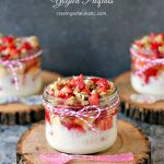 Strawberry and Banana Yogurt Parfaits served in mason jars on wood trivets with colourful spoons resting on them.