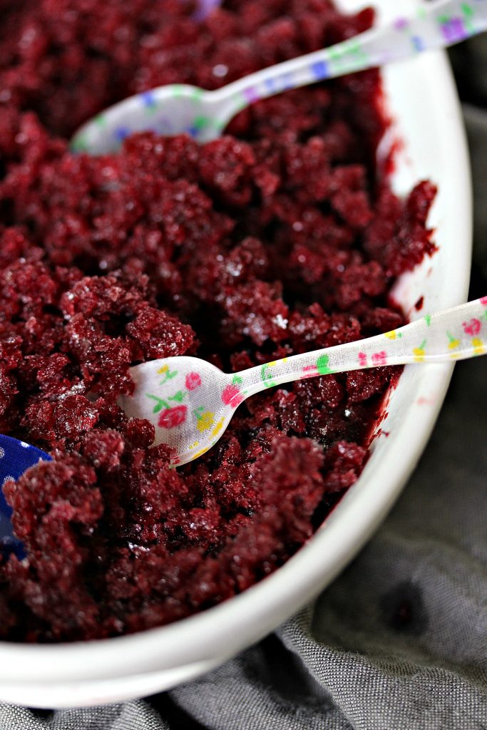 Black cherry granita in a white bowl with multi-coloured spoons. 