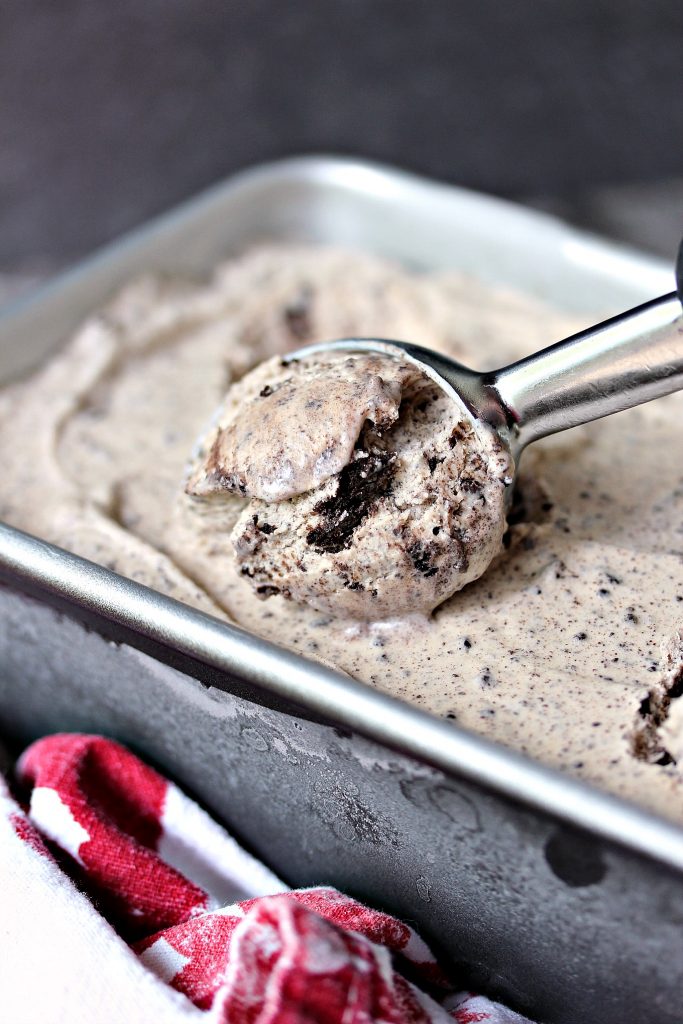 No churn cookies and cream coffee ice cream in a metal pan on a red and white napkin with a scoop being taken out using a metal ice cream scoop. 
