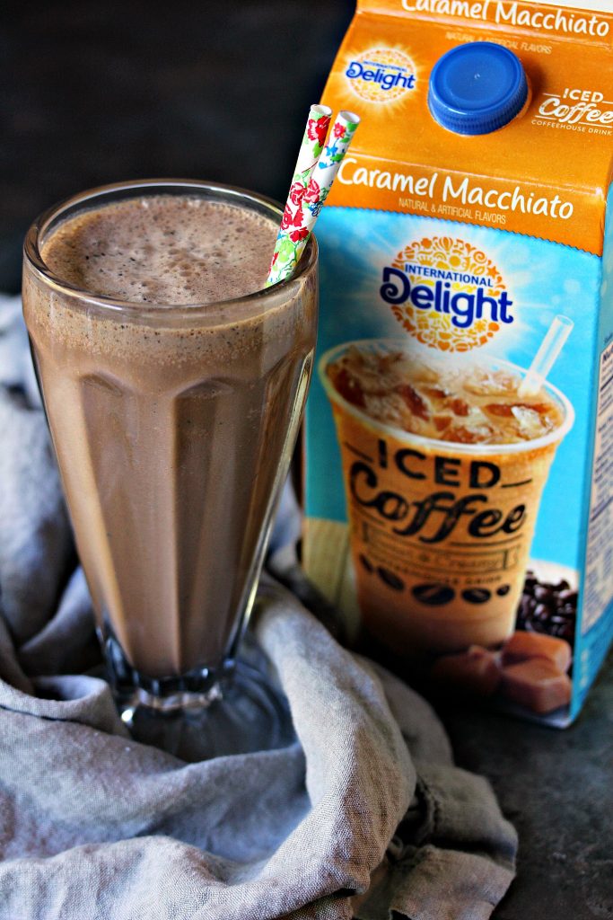 Caramel Macchiato Iced Coffee Chocolate Milkshakes in a milkshake glass on a grey napkin with a carton of International Delight in the background. 