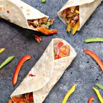 chicken fajitas on a grey counter with cut up peppers scattered around