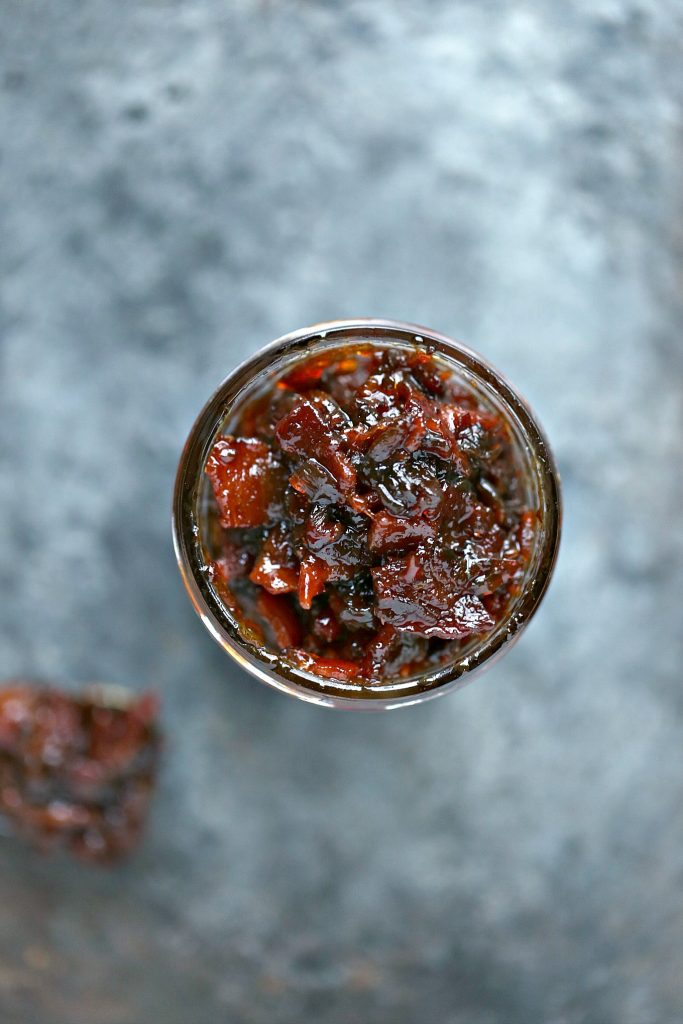 Bacon Jam in a mason jar with a spoonful taken out and resting on a counter.