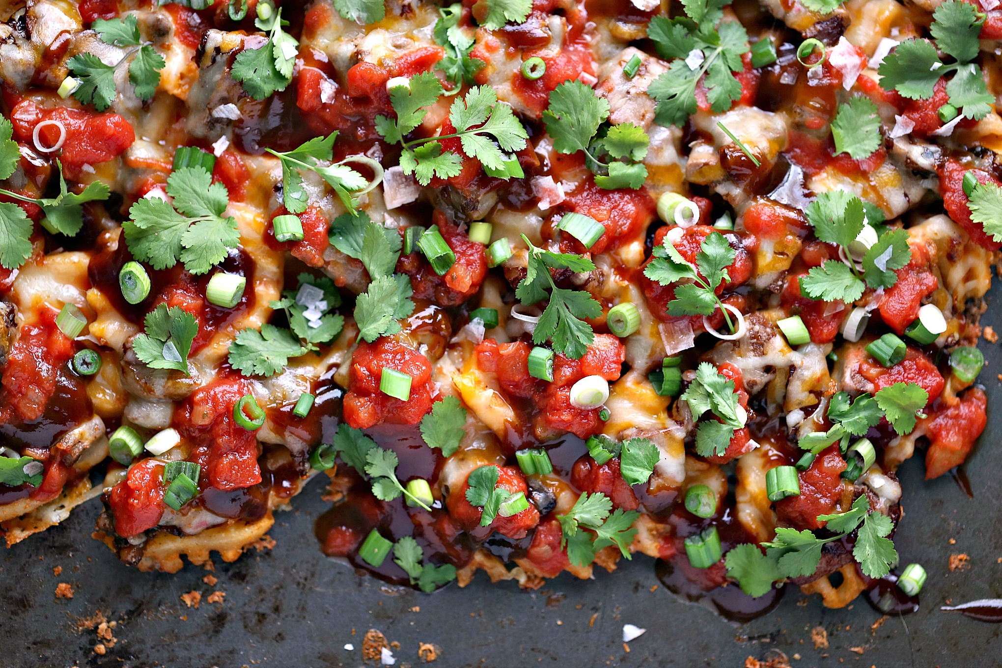 Sheet Pan Steak and Waffle Fry Nachos from cravingsofalunatic.com- These loaded nachos are made with waffle fries, steak and Tex-Mex cheese then topped with barbecue sauce, salsa, onions, and cilantro. All cooked on a sheet pan to make clean up a snap. 