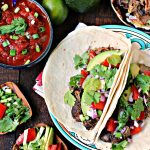 Sweet and Spicy Slow Cooker Carnitas served on tortillas with ingredients scattered around.