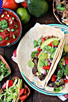 Sweet and Spicy Slow Cooker Carnitas served on tortillas with ingredients scattered around.