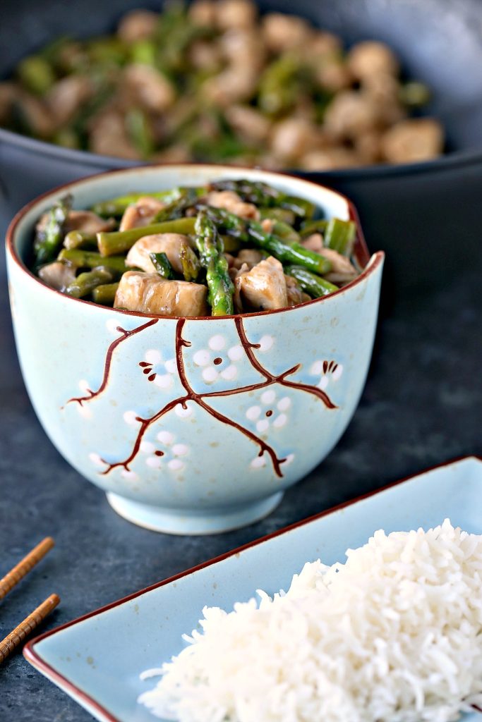 Chicken and asparagus stir fry served in stir fry bowls and plates with white rice, wok is in the background. 