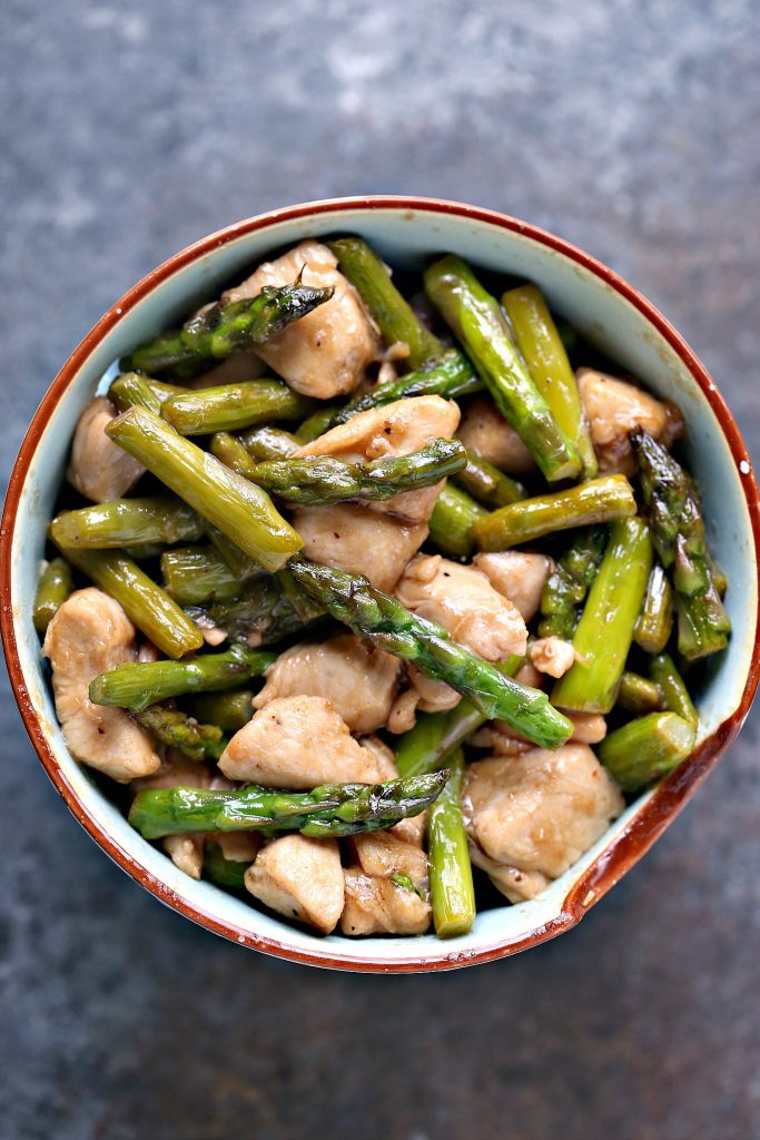 Overhead image of chicken and asparagus stir fry in a bowl on grey counter. 