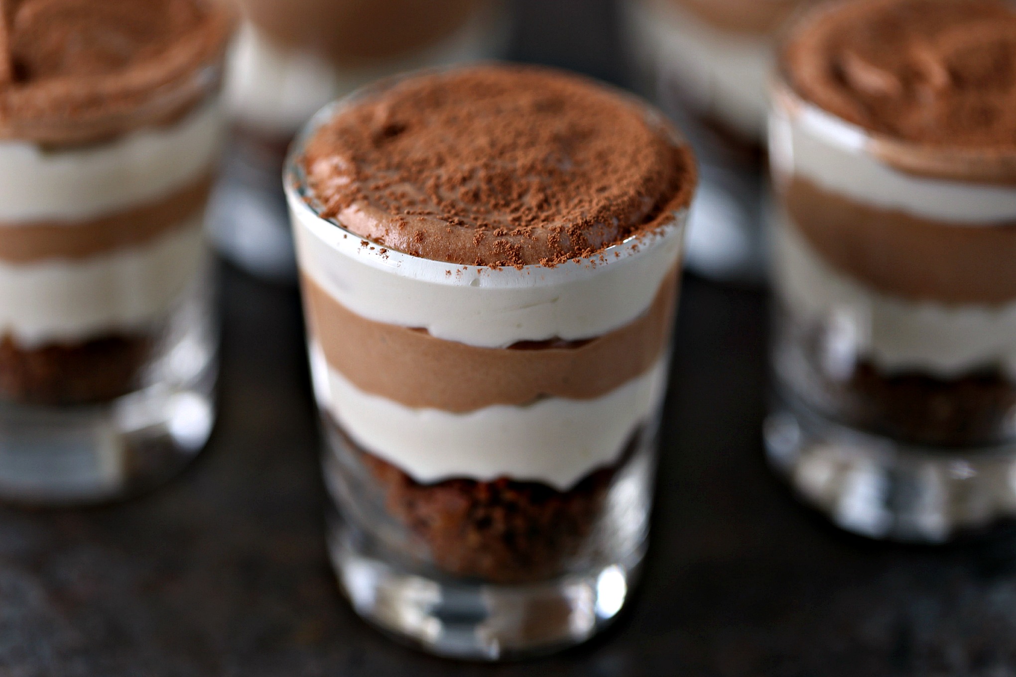 layered No Bake Chocolate and Coffee Mini Cheesecakes in shot glasses sitting on a dark table 