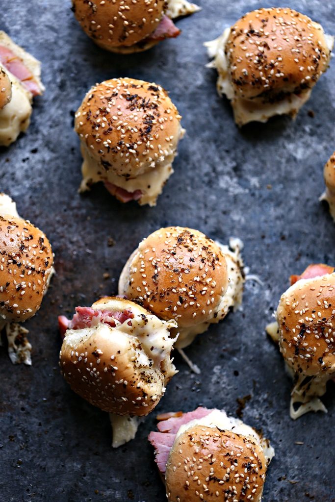 Overhead image of ham and cheese sliders pulled apart and resting on a dark counter. One slider is on it's side.
