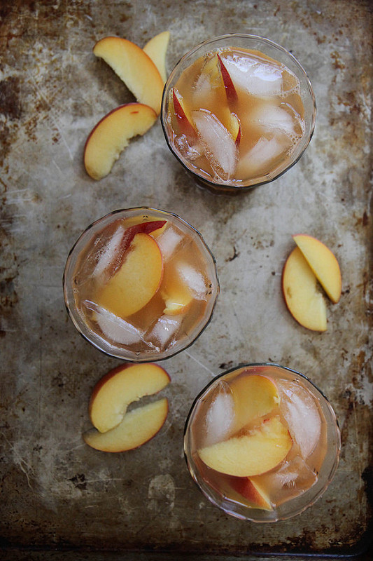 overhead image of Peach Ginger and Bourbon Iced Tea on a tray with sliced peaches scattered around. image by from Heather Christo 