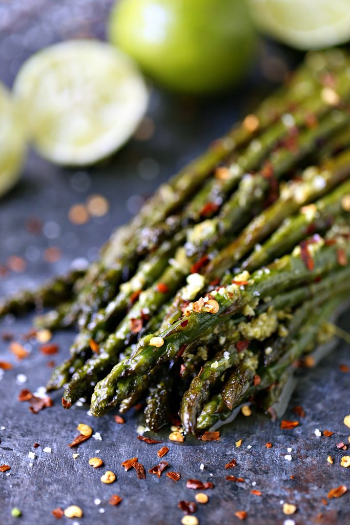 Skillet Asparagus cooked with lime butter piled on a dark counter with red pepper flakes over it and limes in the background. 