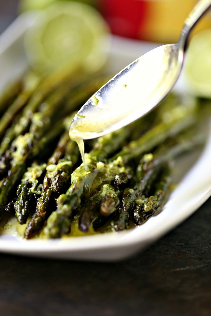 Skillet Asparagus in a white dish with a spoonful of lime butter being drizzled over top. 