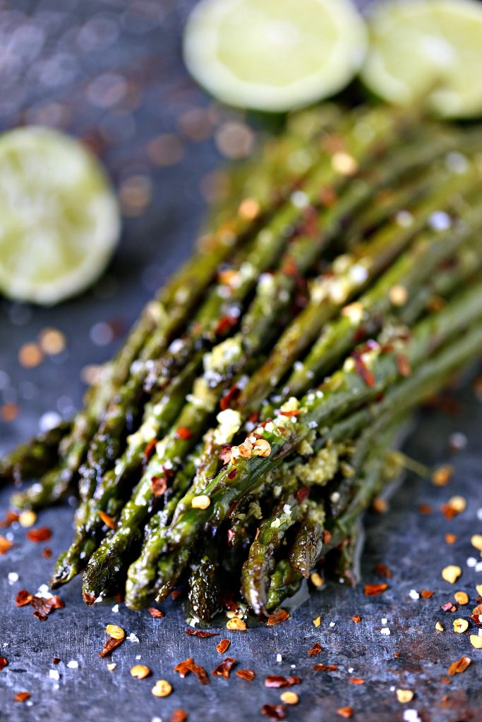 Skillet Asparagus with Lime Butter piled on a dark counter with red pepper flakes sprinkled over top and limes in the background.