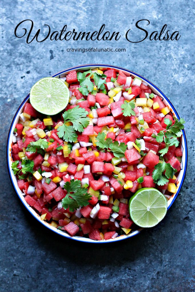 Watermelon salsa in a bowl on a dark surface. Two lime halves are on top of the salsa. Recipe name and blog name text are at the top of the image in black font. 