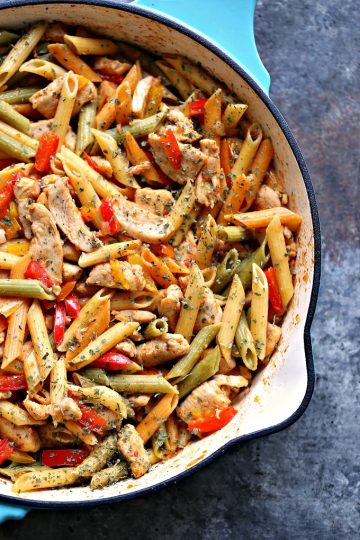 Close up photo of chicken and vegetable pasta in a blue cast iron skillet.