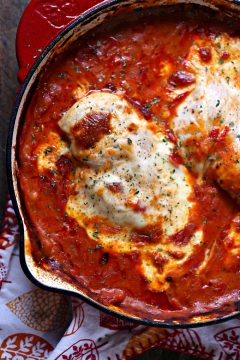 saucy mozzarella chicken baked in a red skillet sitting on a wood table with a napkin nearby