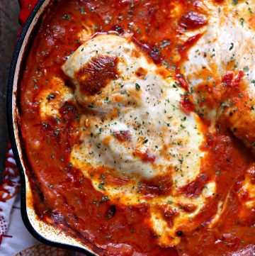 saucy mozzarella chicken baked in a red skillet sitting on a wood table with a napkin nearby