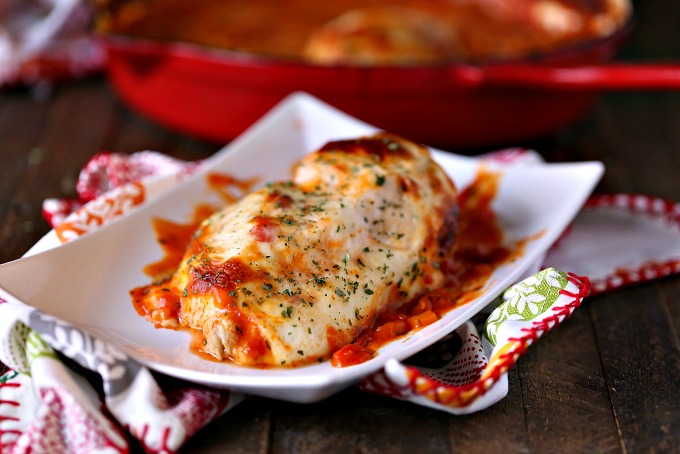saucy mozzarella chicken bake on a white plate served on a napkin with leaves on it with a red skillet filled with saucy mozzarella chicken in background