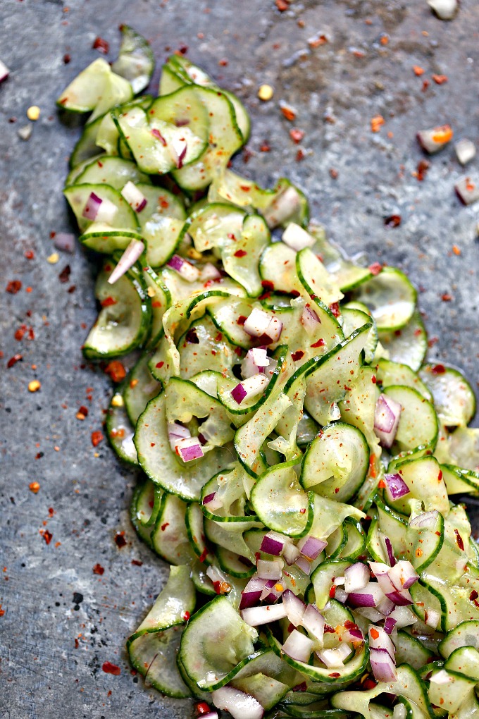 overhead image of Thai cucumber salad spread out on a grey platter and garnished with shallots and red pepper flakes