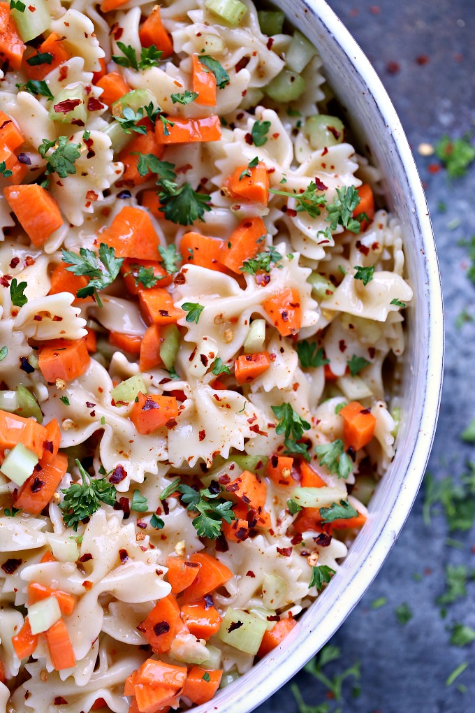 close up overhead image of Bow Tie Pasta Salad in a white serving bowl on a dark background with fresh parsley sprinkled around 