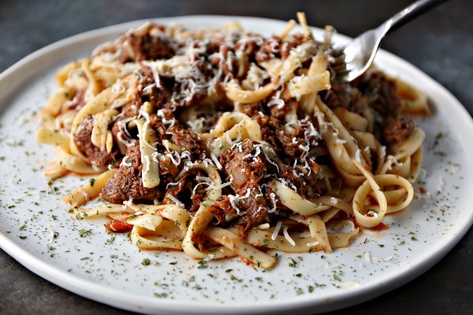 close up image of slow cooker short rib ragu served on a white plate and sprinkled with parmesan cheese