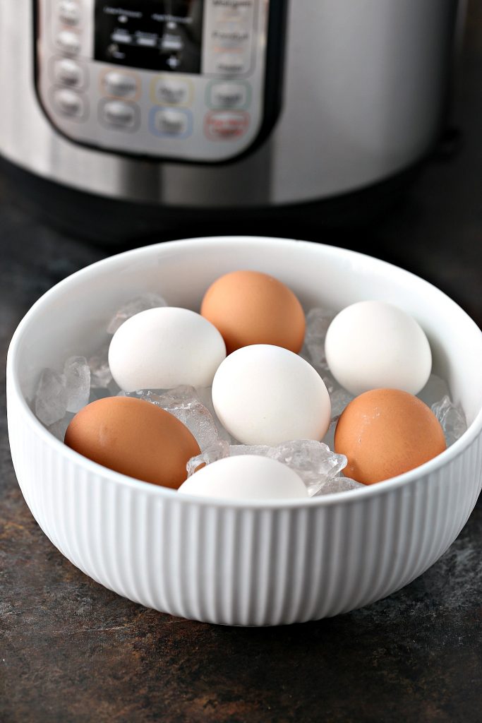 Hard boiled eggs in an ice bath inside in a large white bowl. Instant pot is in the background. 