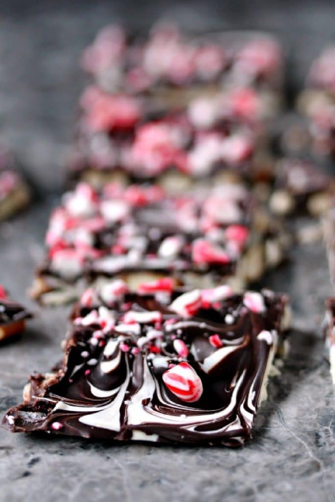 Pieces of pretzel bark topped with chopped peppermint cooling on a grey marble counter. 