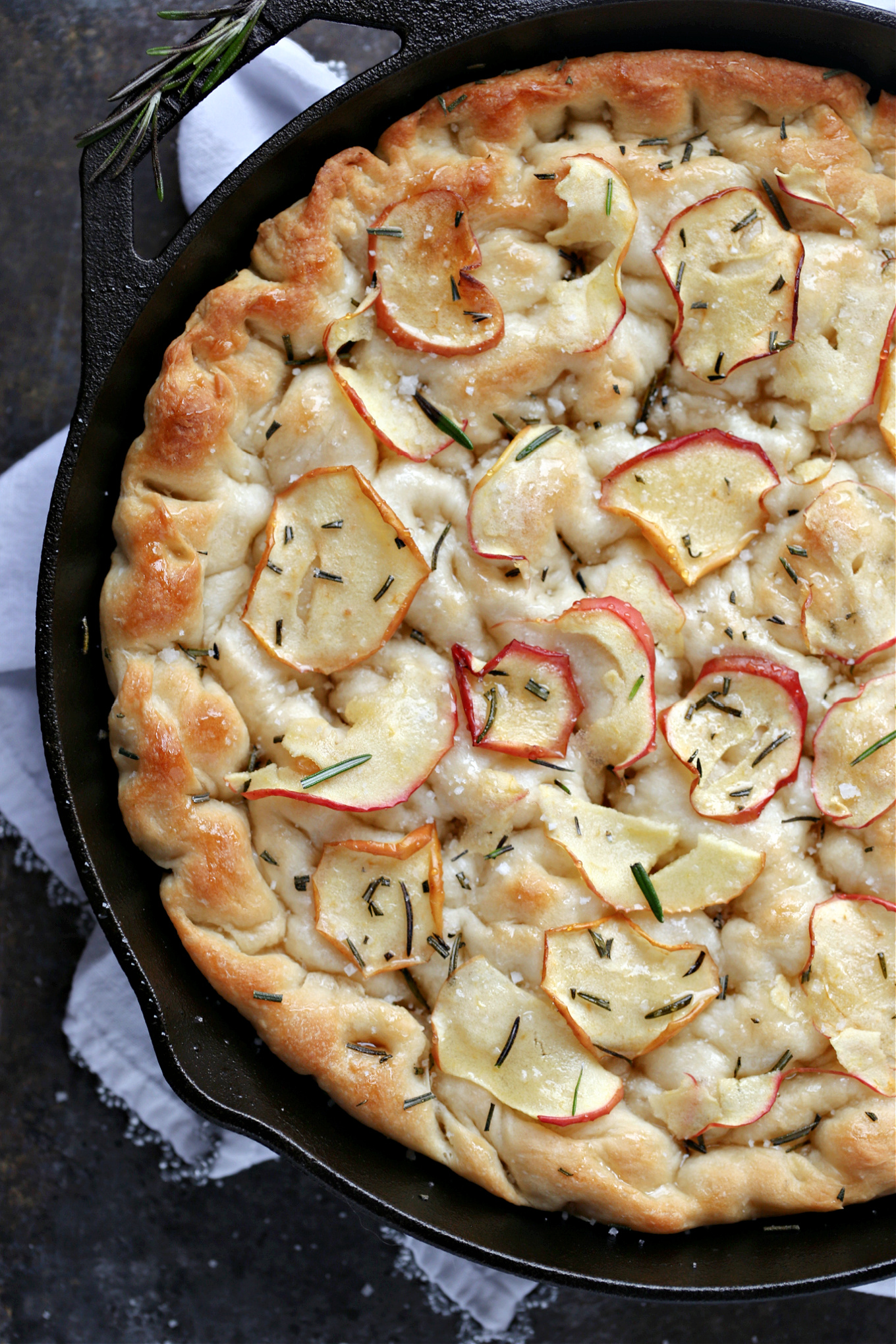 overhead image of apple rosemary focaccia in a black cast iron pan on a white napkin