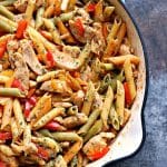 Overhead image of a chicken veggie pasta in a large skillet on a greyish counter.