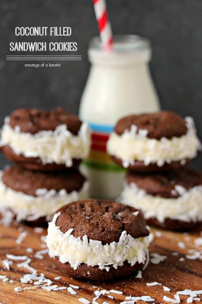 Coconut Filled Sandwich Cookies spread randomly on a wooden board with a glass of milk in the background.