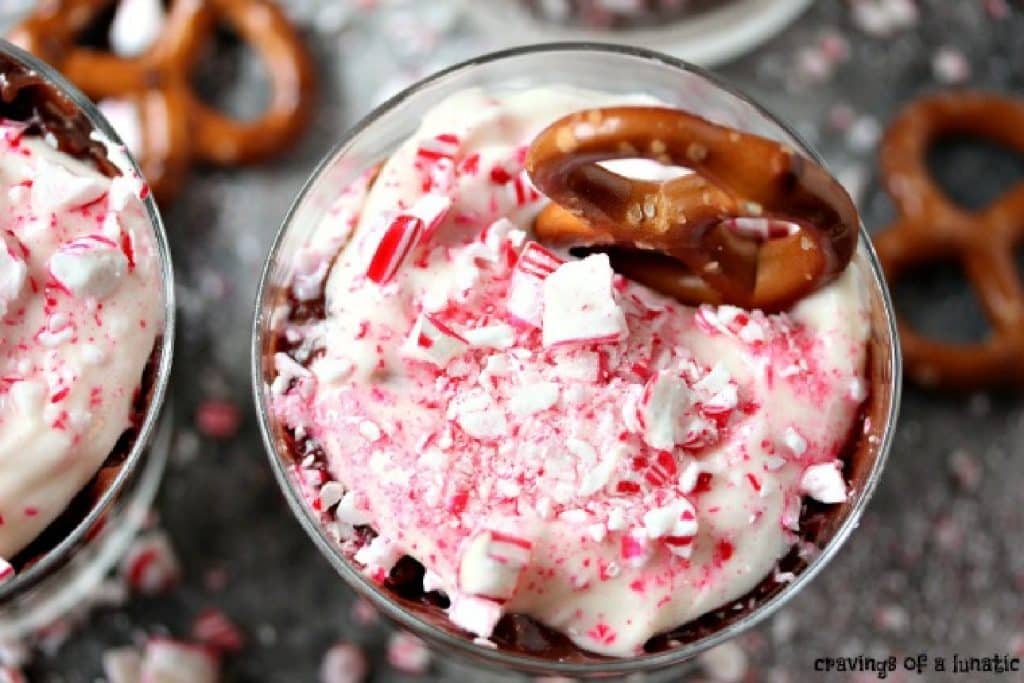 An overhead image of peppermint dip in a clear glass dish with a pretzel inside of it and a pretzel on the counter next to the dish.