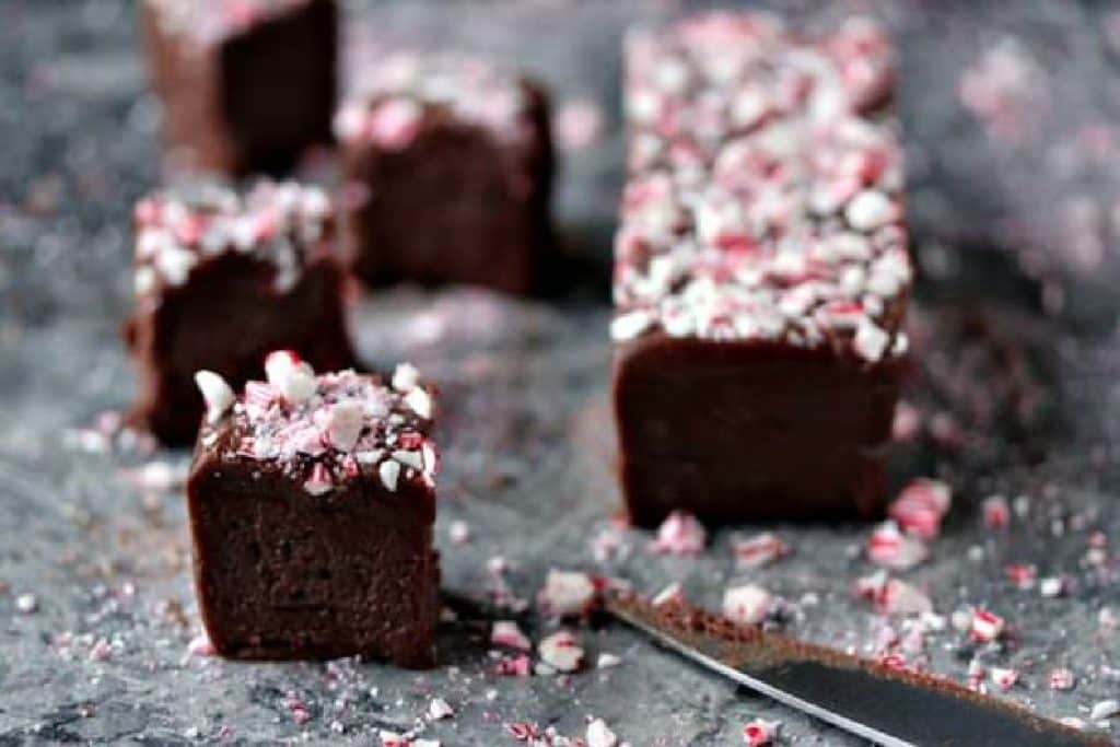 Pieces of chocolate peppermint fudge on a grey marble counter with a slab of the fudge off to the side on the right.