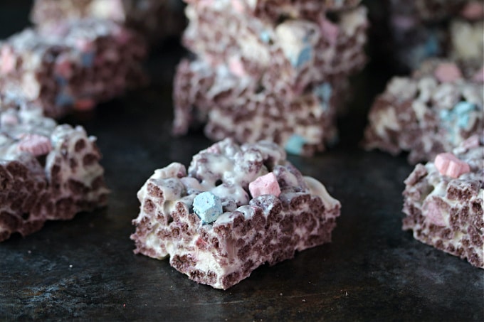 Boo berry krispies cut into pieces and cooling on a dark counter.