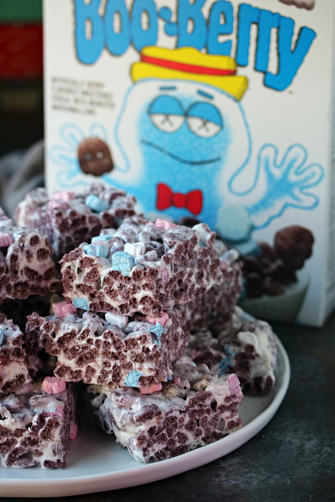 Boo berry krispie treats served on a white plate with a box of Boo Berry cereal in the background.