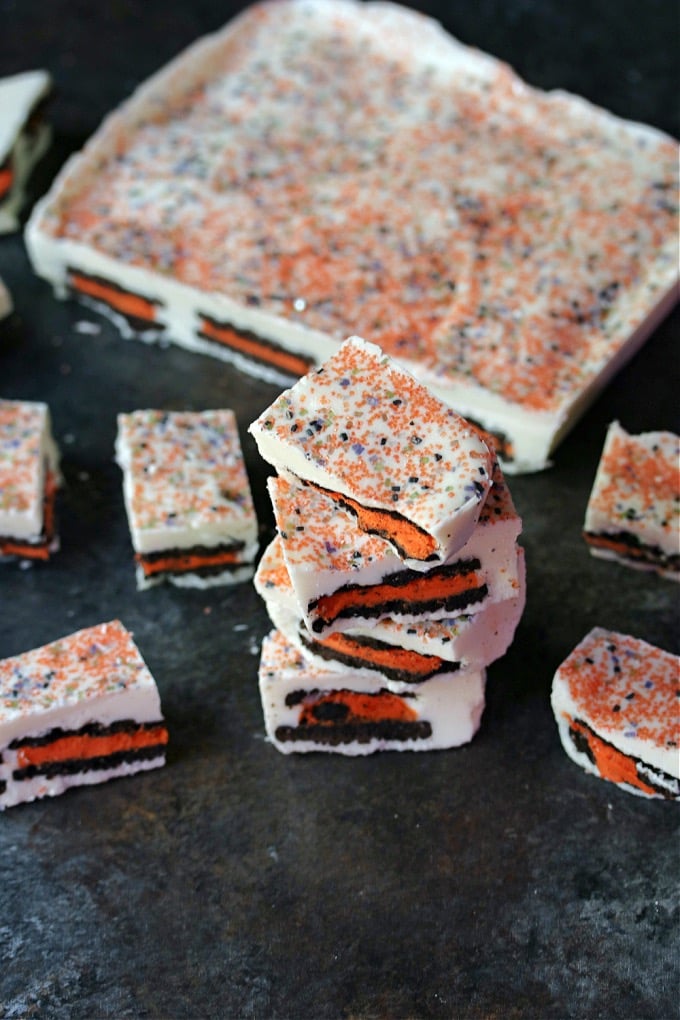 Halloween oreo bark made with white chocolate and orange filled oreos, bark is stacked on counter with a slab of bark in the background.