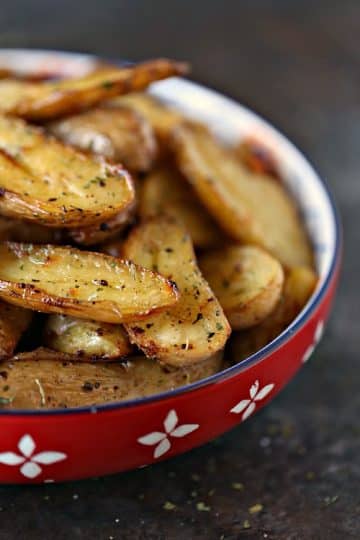 Lemon roasted sliced fingerling potatoes cooked to perfection and served in a large red and white bowl on a dark counter.
