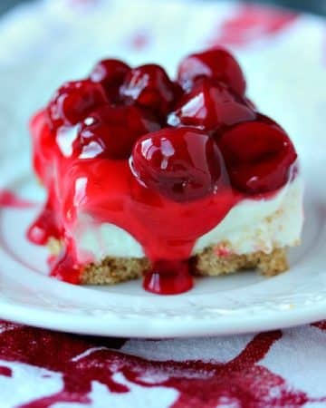 No Bake Cherry Cheesecake Bars served on a white plate on a red and white napkin.
